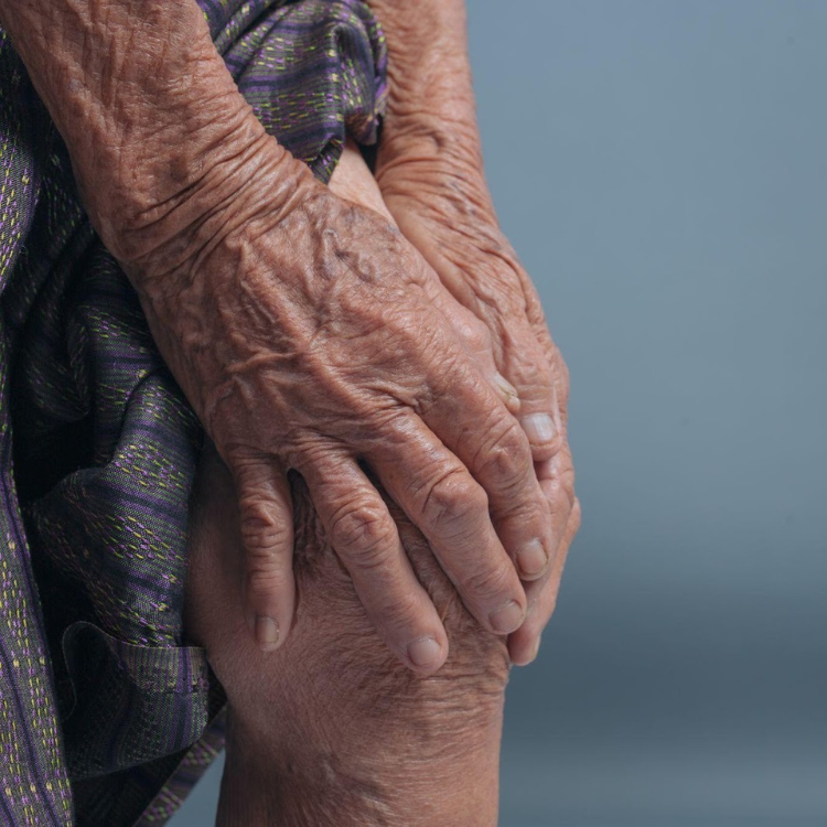 Idosa com dores nas pernas, a colocar as mãos no joelho