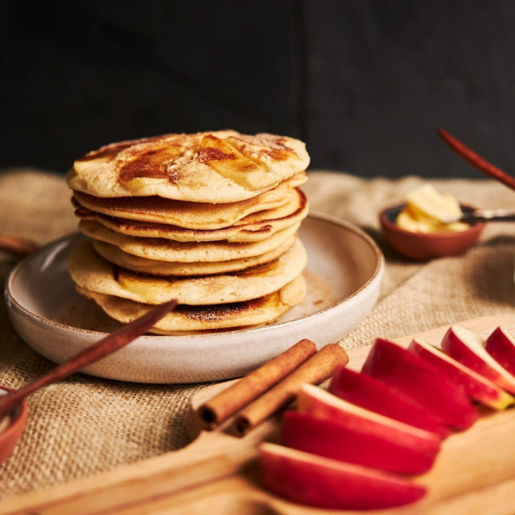 Torre de panquecas de aveia e maçã em cima de um prato com maçã e canela a decorar